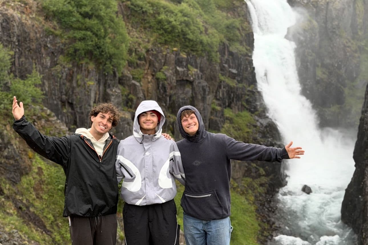 Three friends with arms wide open in front of a roaring Icelandic waterfall